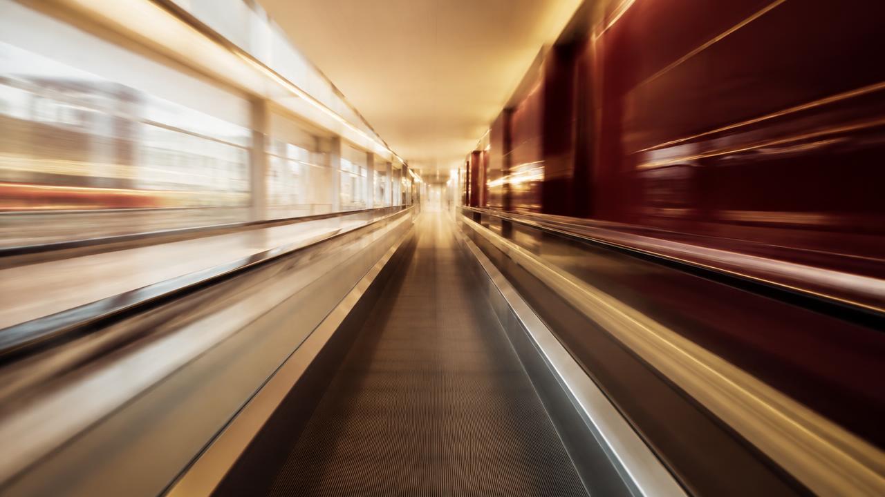 A blurred moving walkway rushing through a long corridor